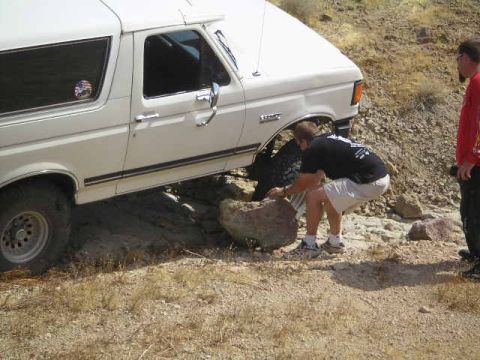 1988 Ford Bronco - A man attempts to free a white 1988 Ford Bronco that is stuck on a rocky incline, off-road trail.