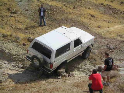 1988 Ford Bronco - A white 1988 Ford Bronco is captured off-roading on a rocky, dry hillside with onlookers present.