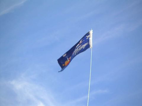 1988 Ford Bronco - A flag with text and graphics flies against a bright blue sky with wispy clouds.