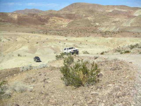 1988 Ford Bronco - Two vehicles navigate a dusty desert terrain under a clear blue sky.