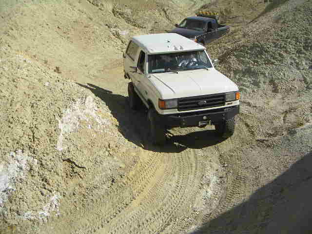 White Ford Bronco driving on a dirt trail with another truck behind it