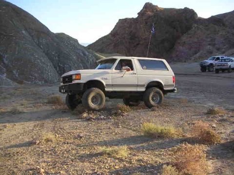 1988 Ford Bronco - A white Ford Bronco is parked in a desert landscape with mountains in the background.