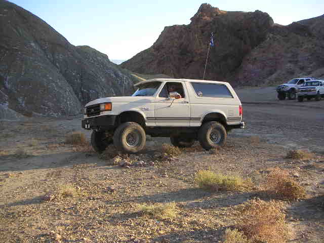 White Ford Bronco with off-road tires parked on a dirt road in a desert landscape