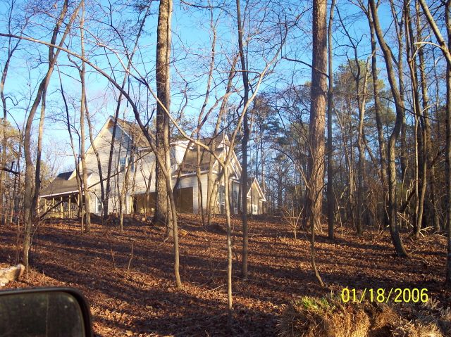 house in woods with bare trees and fallen leaves