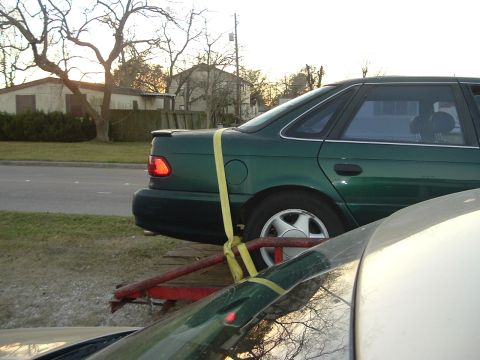 1993 Ford Taurus - A green sedan is secured with yellow straps to a trailer, viewed from the rear quarter.
