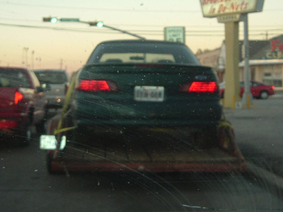 1993 Ford Taurus on a trailer, rear view. Another red vehicle is visible to the left