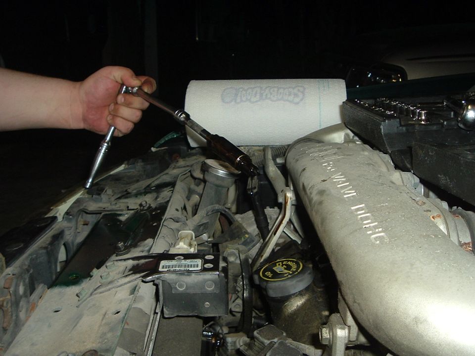 hand using socket wrench on engine part, paper towel in background