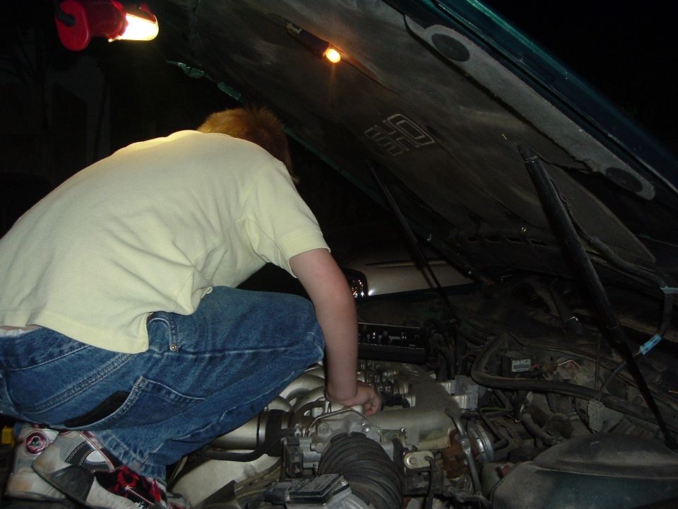 Person working on engine under hood, dark scene with work light
