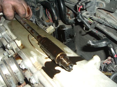 1993 Ford Taurus - A mechanic's hand holds a spark plug coated in dark oil, positioned over a greasy engine part.