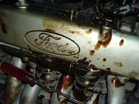 1993 Ford Taurus - A close-up shows a Ford engine component stained with oil, with a screwdriver resting on it.
