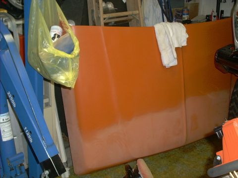 1978 Ford Bronco - A car hood, painted orange, sits in a garage with a yellow bag of items hanging from a blue hoist.