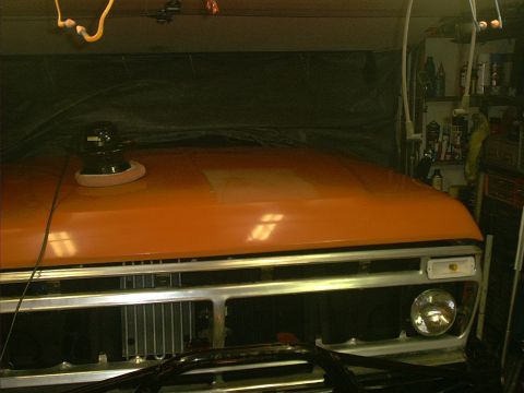 1978 Ford Bronco - A buffer sits on the hood of an orange pickup truck being worked on in a garage.