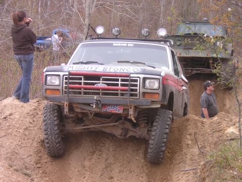 1977 Ford F-150 - A modified Ford Bronco navigates a steep dirt incline, with another vehicle and onlookers nearby.
