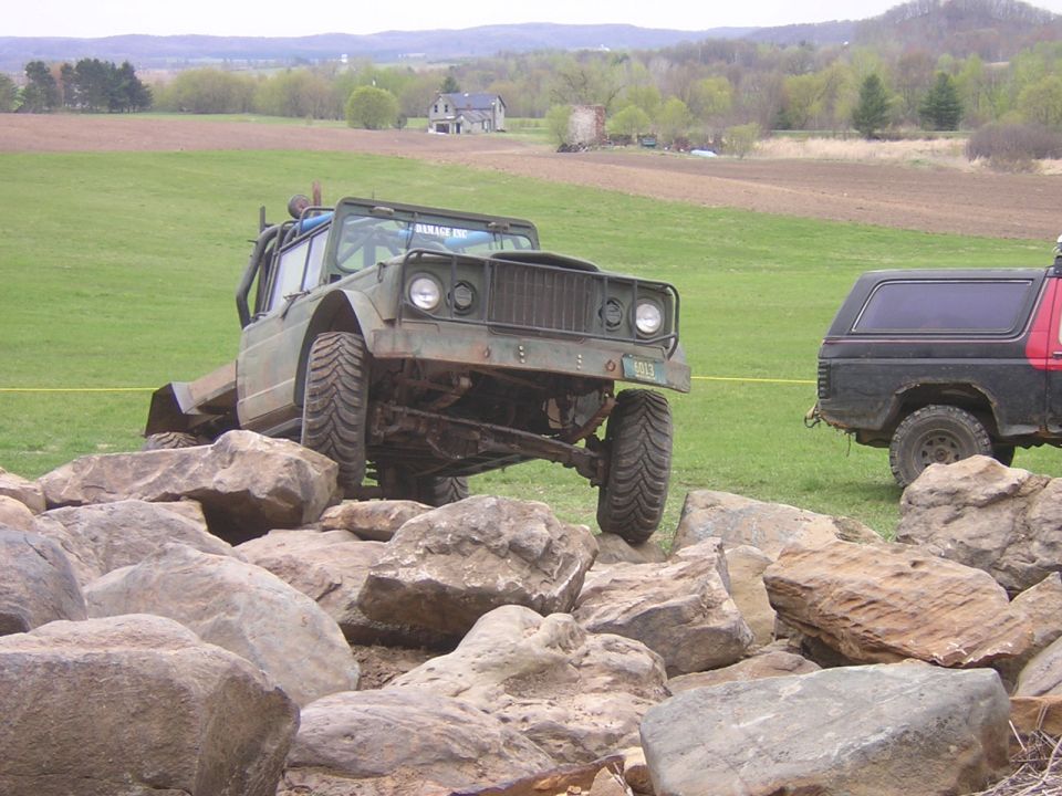 Green Jeep CJ-8 Scrambler on rocks, black SUV in background