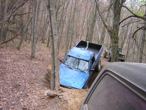 1977 Ford F-150 - Two off-road vehicles navigate a wooded trail, with one truck stuck in a deep ditch.