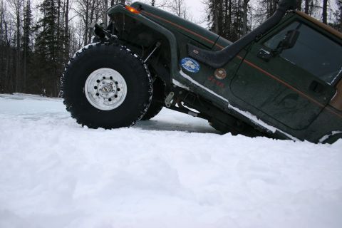 2003 Jeep TJ - A green 2003 Jeep TJ is partially submerged in snow, with its large tires visible.
