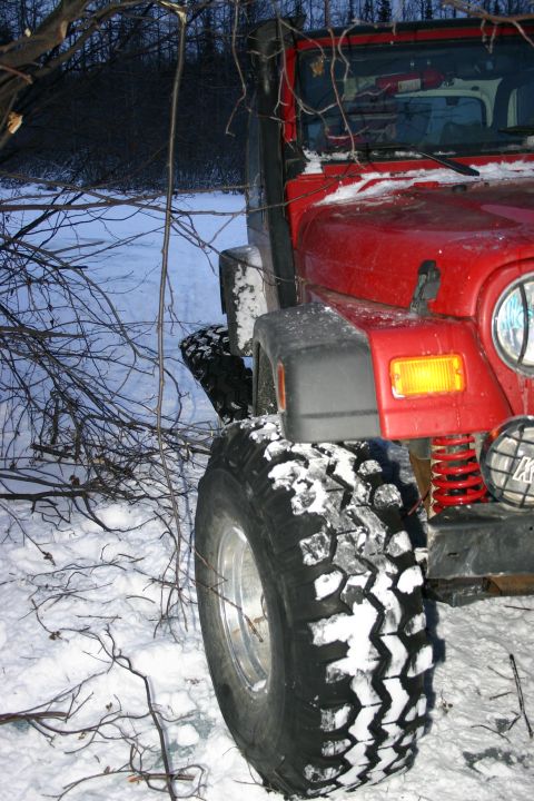 2003 Jeep TJ - A red 2003 Jeep TJ is partially covered in snow, parked near trees in a winter landscape.