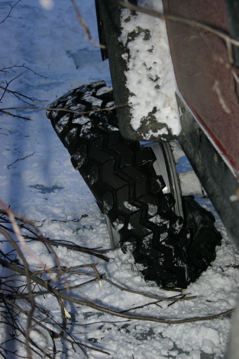 2003 Jeep TJ - A vehicle's tire is partially buried in snow, surrounded by bare branches and wintery ground.
