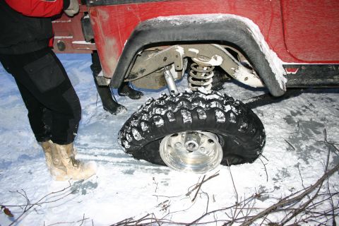 2003 Jeep TJ - A flat tire on a red Jeep is visible in the snow, with a person standing next to it.