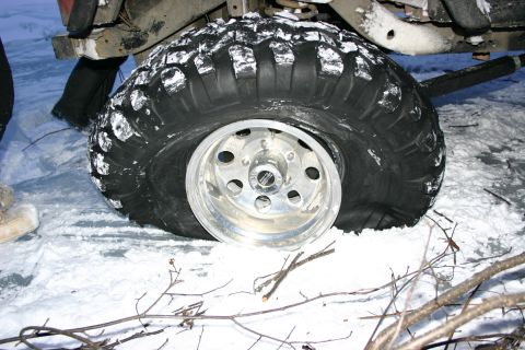 2003 Jeep TJ - A vehicle's flat tire is visible in the snow, with branches scattered around.