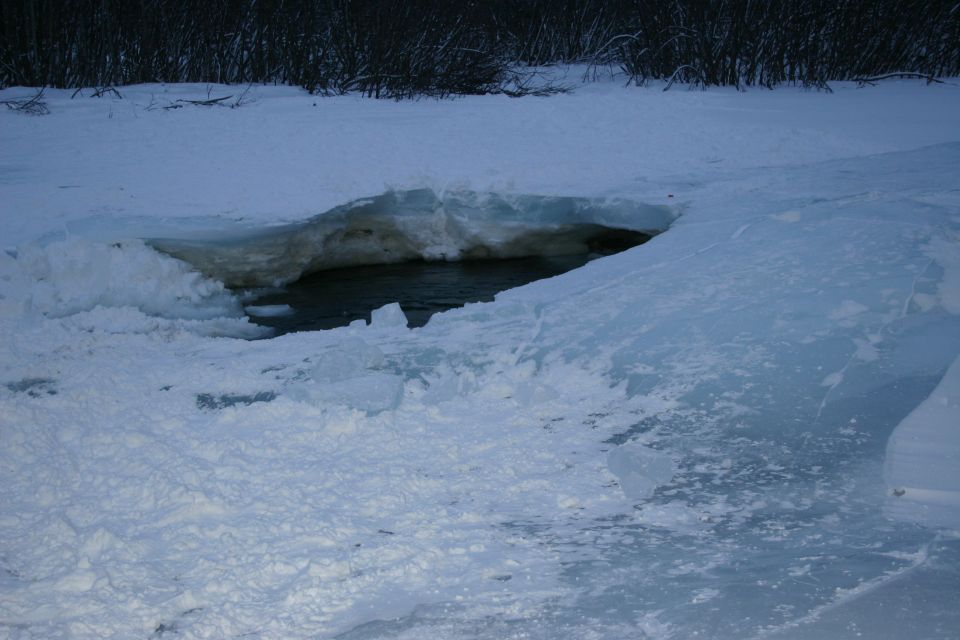 Hole in ice on a frozen body of water with dark trees in the background