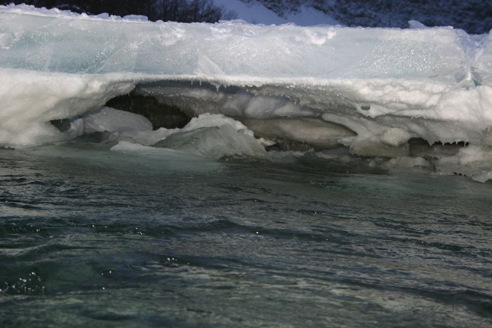 Ice formation over dark water with visible icicles hanging from the ice
