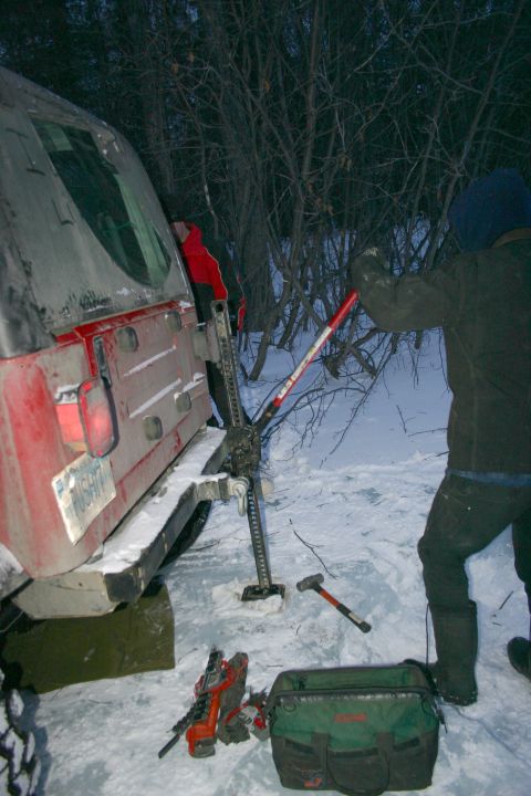 2003 Jeep TJ - A red 2003 Jeep TJ is partially visible in a snowy environment with a jack attached to its rear.
