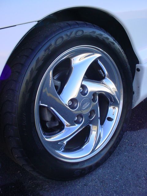 1996 Ford Probe - A close-up shot focuses on the chrome wheel and tire of a vehicle, revealing a Ford emblem on the wheel's hub.