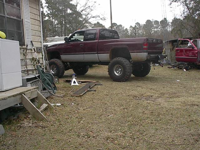 Maroon 2001 Dodge 1500 pickup truck with large tires, parked next to a house