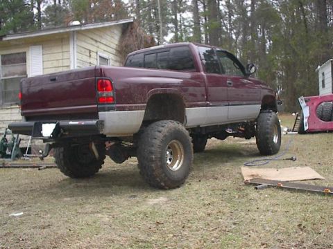 2001 Dodge 1500 - This lifted pickup truck is parked in a grassy area with a house in the background.