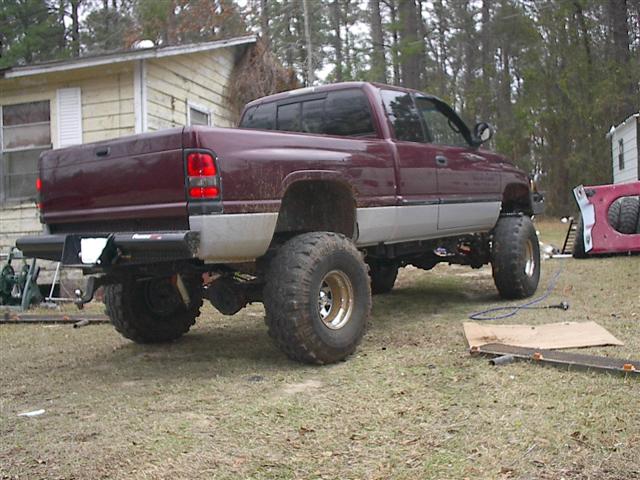Maroon lifted pickup truck parked in a yard, rear view