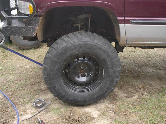 Close-up of a large truck tire and fender. A blue tool is on the ground near the wheel