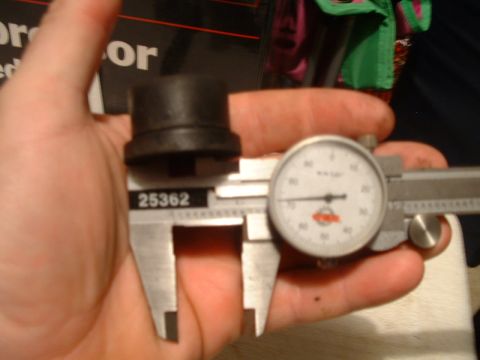 1995 Ford Bronco - A part is being measured with a dial caliper. The part is black and cylindrical with a flange.