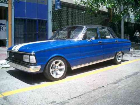 1972 Ford Ranchero - A blue sedan with white racing stripes is parked on a street next to a building.