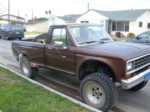 1985 Ford Ranger - A brown pickup truck with a spare tire in the bed is parked on the side of the road.