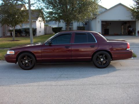 2004 Ford Crown Victoria - A maroon 2004 Ford Crown Victoria sedan is parked on a residential street, its side profile and black aftermarket wheels.