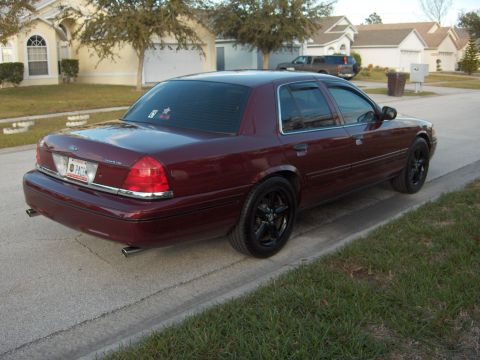 2004 Ford Crown Victoria - A maroon Ford Crown Victoria is parked on a suburban street, showing its rear profile and custom black wheels.