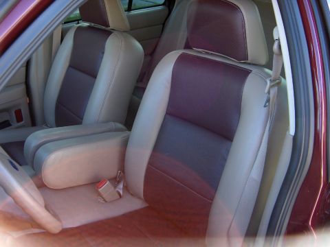 2004 Ford Crown Victoria - The interior of a car shows tan and dark red seats with a tan armrest and seatbelt visible.