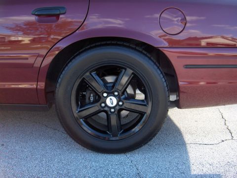 2004 Ford Crown Victoria - The rear wheel and fender of a maroon 2004 Ford Crown Victoria are shown with black rims.