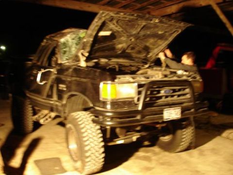 1990 Ford Bronco - A black 1990 Ford Bronco is shown with its hood open, revealing the engine bay and a person working on it.