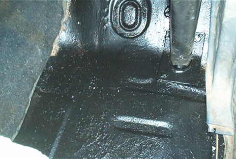1986 Ford Bronco - Close-up of a vehicle's interior floor, showing areas of rust and recent black paint application.