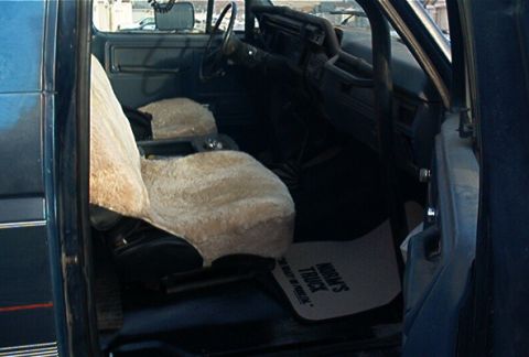 1986 Ford Bronco - Interior of a blue truck, possibly from the 1980s, showing seat covers and a floor mat.