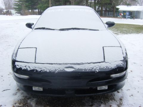 1995 Ford Probe - A black Ford Probe sits covered in snow, its front end and pop-up headlights visible.
