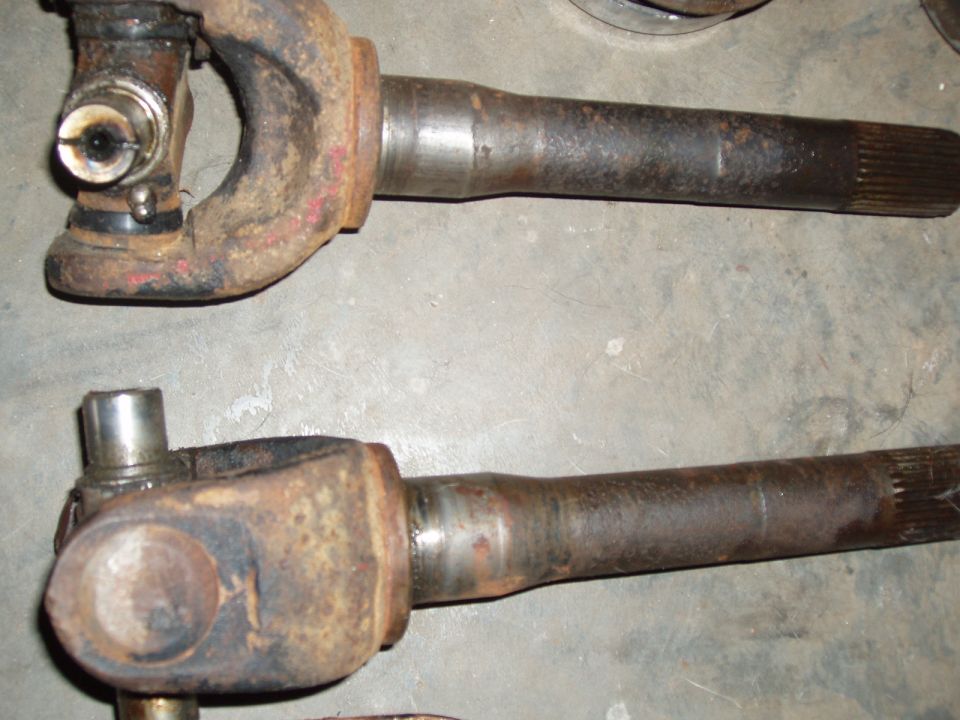 Two rusty front axle shafts with universal joint yokes laid on a concrete floor