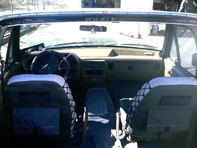 Interior of a Bronco looking forward at tan dash, steering wheel, and seat-covered bucket seats with netting