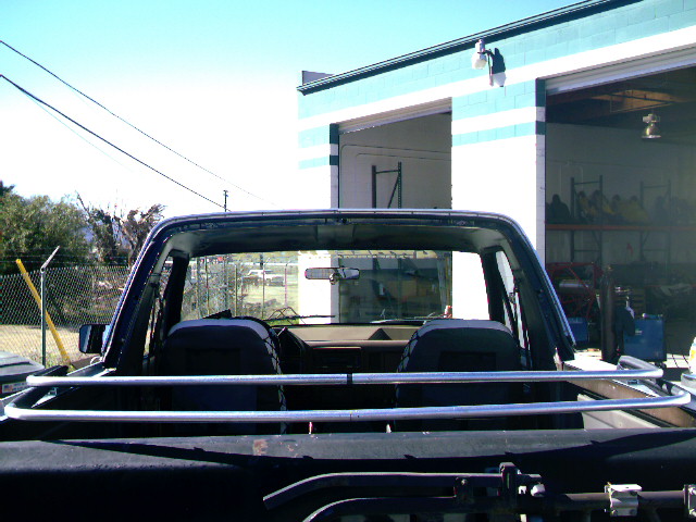 Rear view of a topless dark blue Bronco showing roll bar, seats, and chrome rails, parked outside a shop