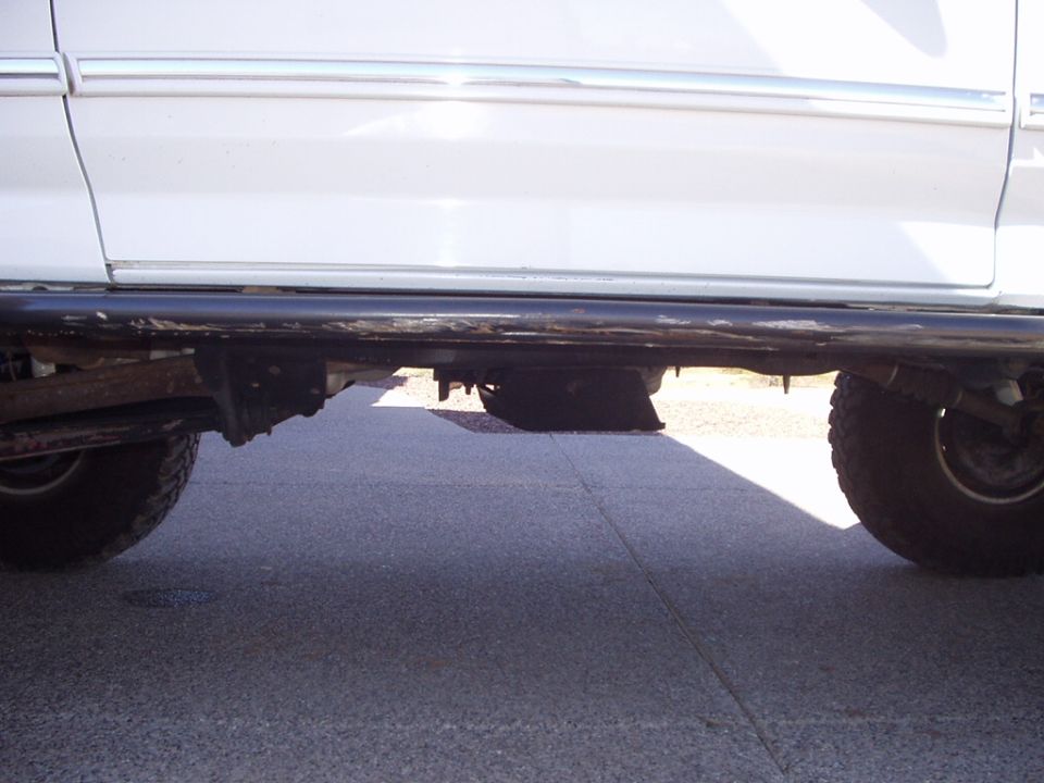 Scraped black rock slider bar under the rocker of a white Ford truck on concrete
