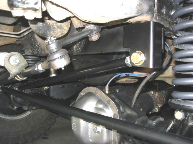 Undercarriage showing black track bar mount bracket, coil spring, steering linkage and axle differential.