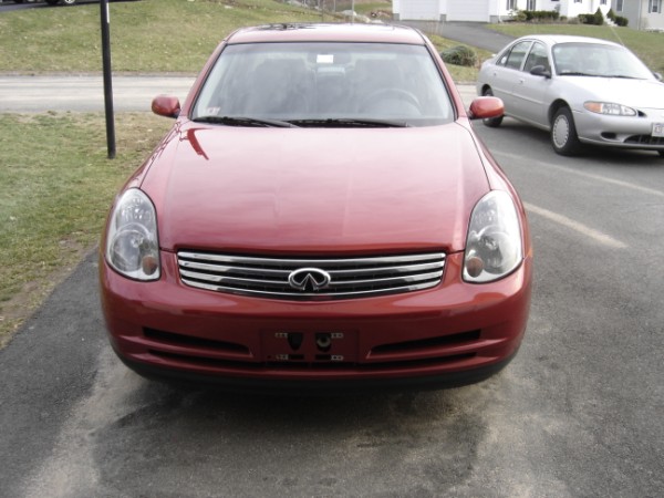 Front view of red Infiniti sedan with chrome grille and Infiniti logo. Silver sedan in background