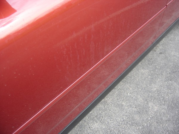 Close-up of a dusty red car door panel with a black trim piece along the bottom